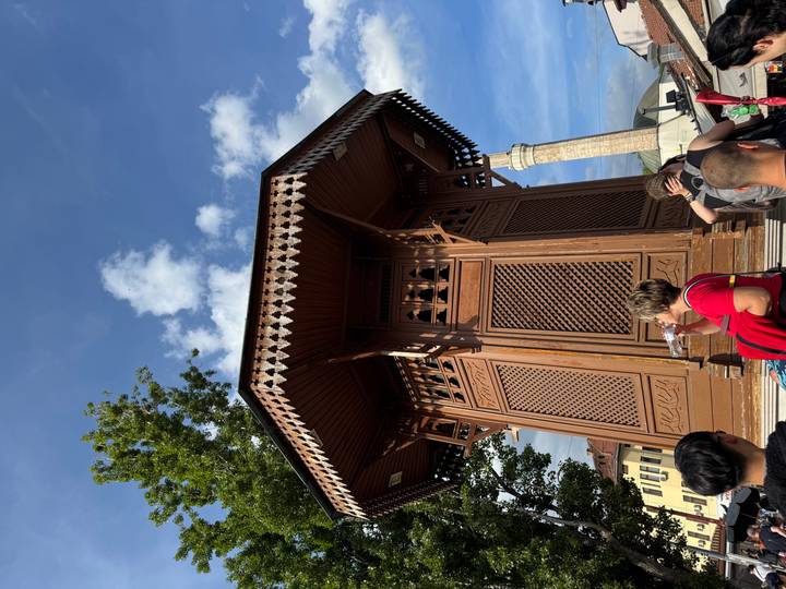 Tourists gather around the wooden Sebilj Fountain in Sarajevo’s old bazaar on a sunny afternoon.