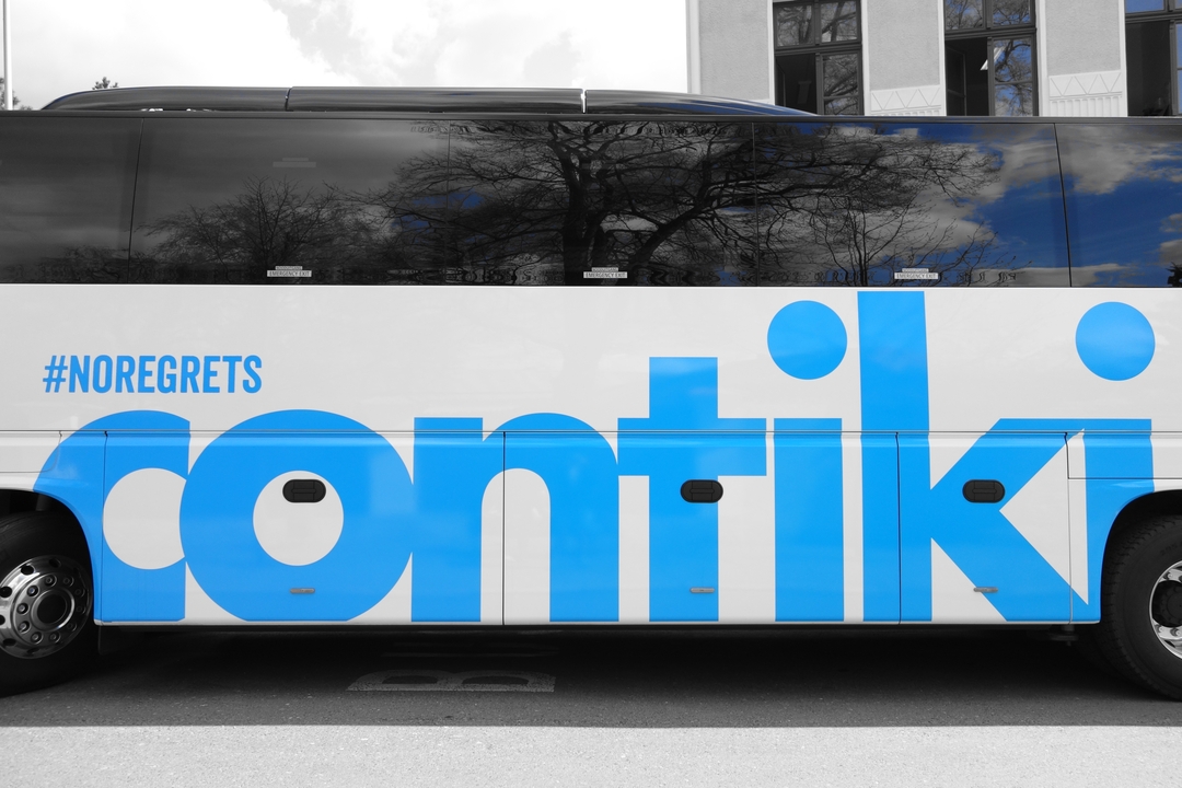 Bus de tourisme portant la marque #NORegrets garé près d'arbres.