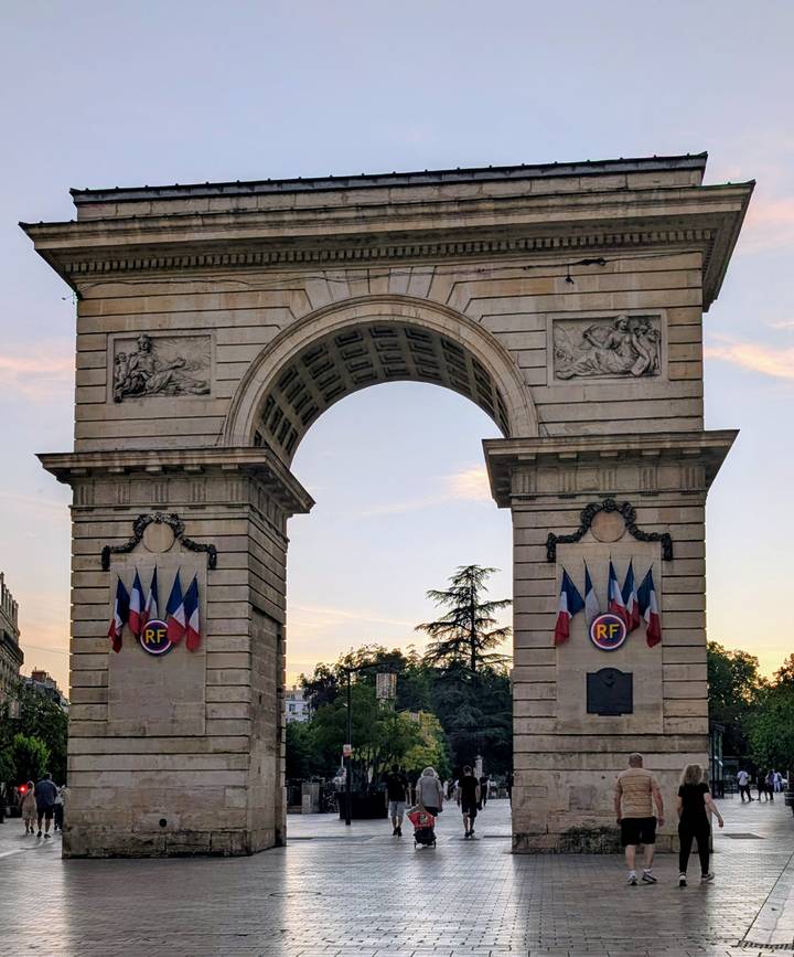 Triumphal arch Porte Guillaume adorned with French flags at dusk in Dijon
