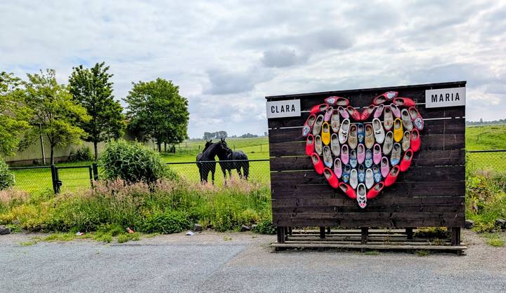 Outdoor display of colorful wooden clogs arranged in a heart shape on a farm fence