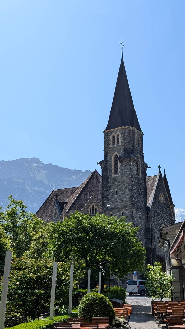 Stone church with mountain backdrop under clear summer sky
