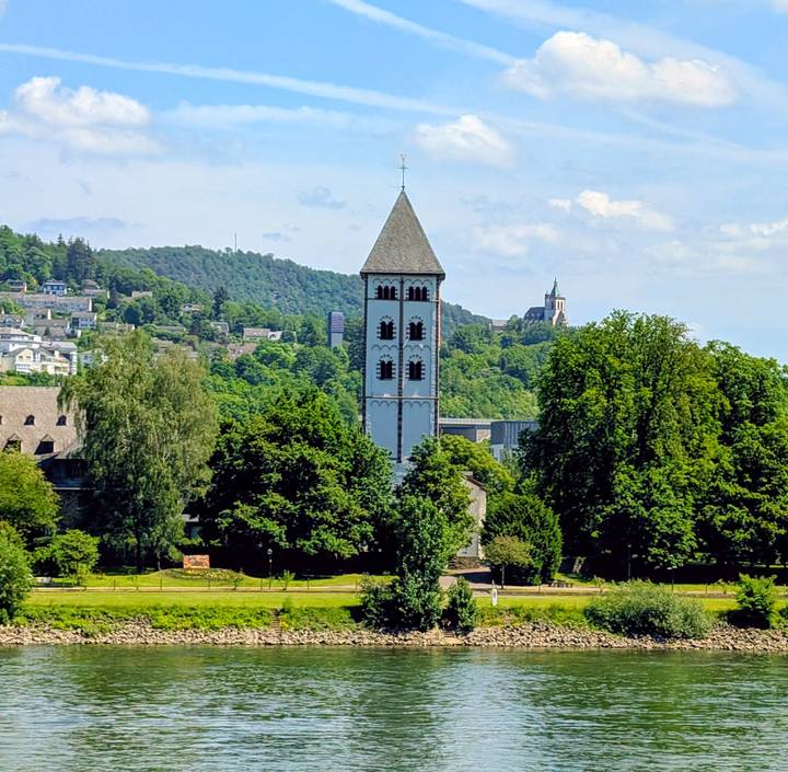 Slim historic tower rising above treetops in a lush riverside landscape