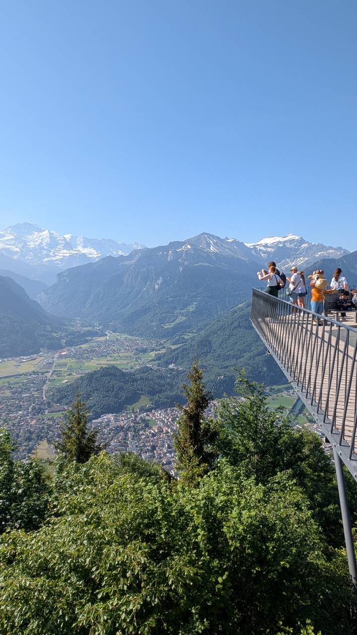 Visitors on steel viewing platform overlooking broad Swiss valley and snow peaks