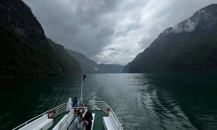 Passenger boat cruising between steep misty mountains on Norway’s Sognefjord.