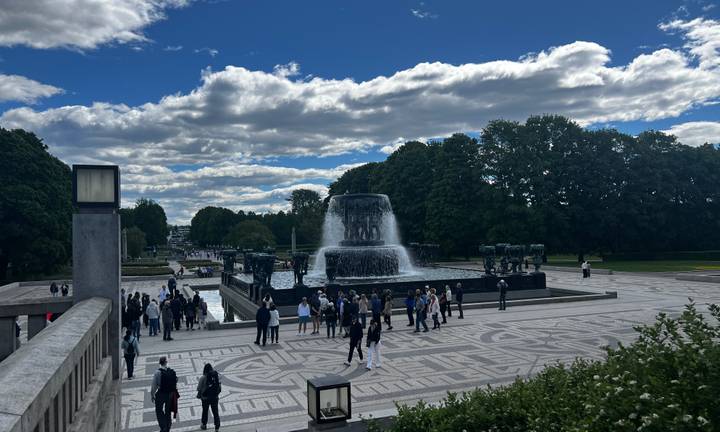 Crowds gather around Vigeland Park’s grand fountain under partly cloudy skies in Oslo.