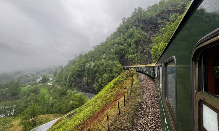 Green train winding through misty mountains on Norway’s famous Flåm Railway.