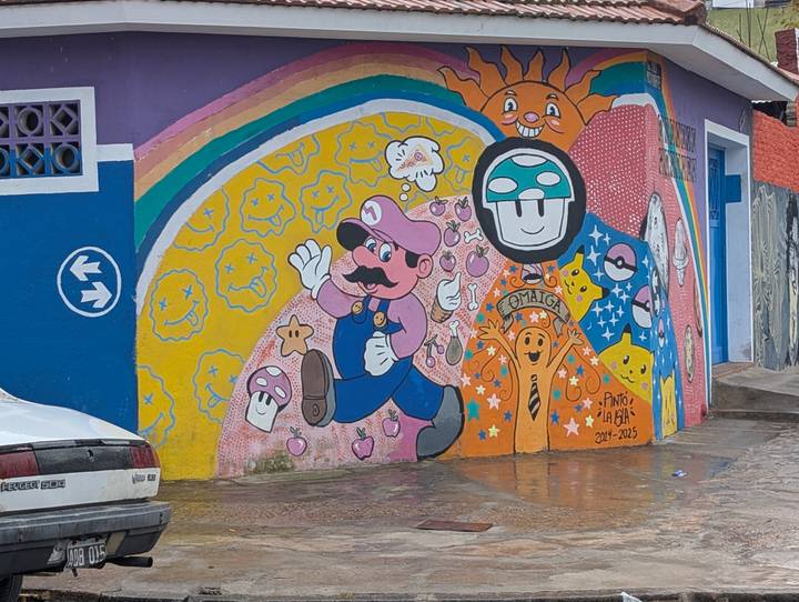 Vibrant street mural featuring video-game characters like Mario and Toad painted on a colorful wall along a wet city street.