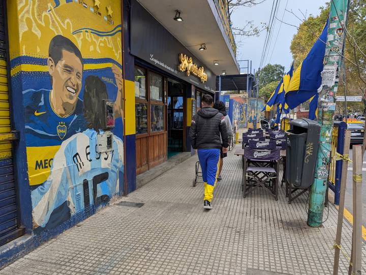 Pedestrian passes a restaurant decorated with a vivid Boca Juniors soccer mural and blue-and-yellow flags in Buenos Aires.