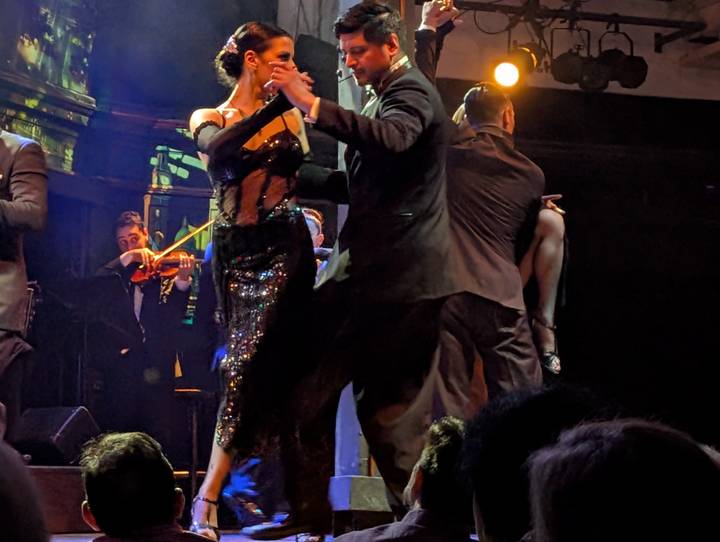 Elegant couple performs an energetic tango on stage accompanied by live musicians during an evening show.