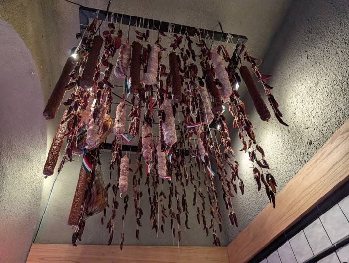 Bunches of cured sausages and dried chilies hang from the ceiling of a rustic delicatessen.