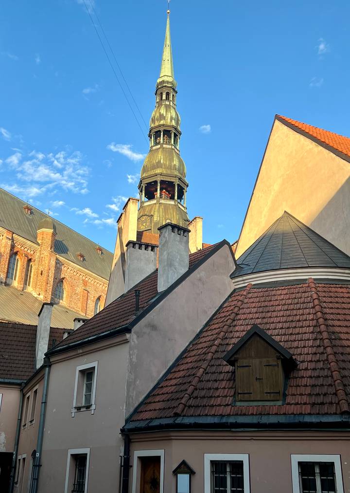 Sunlit view of Riga Cathedral tower framed by rooftops and warm evening light.