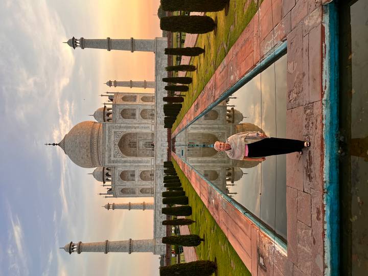 Traveler stands in front of the Taj Mahal at sunrise, with perfect reflection in the water channel.