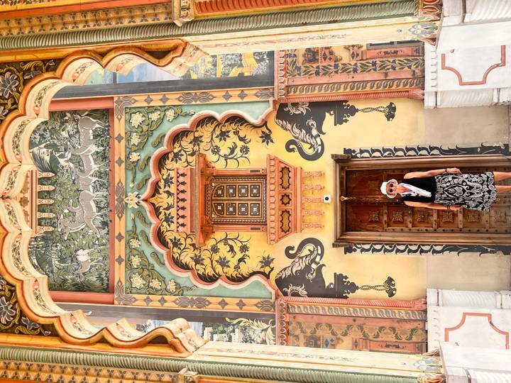 Woman stands before a vividly painted doorway with peacock and floral motifs at Jaipur City Palace.