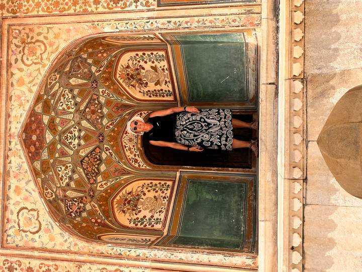 Traveler framed in an ornate archway with detailed frescoes and green painted panels at Amber Fort.