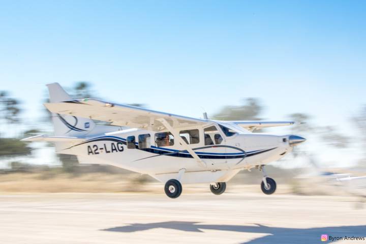 Small white safari aircraft taking off from a dirt airstrip with blurred background.