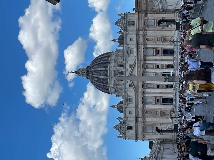 Crowds gather in St. Peter’s Square with the grand dome of St. Peter’s Basilica rising against a bright blue sky.