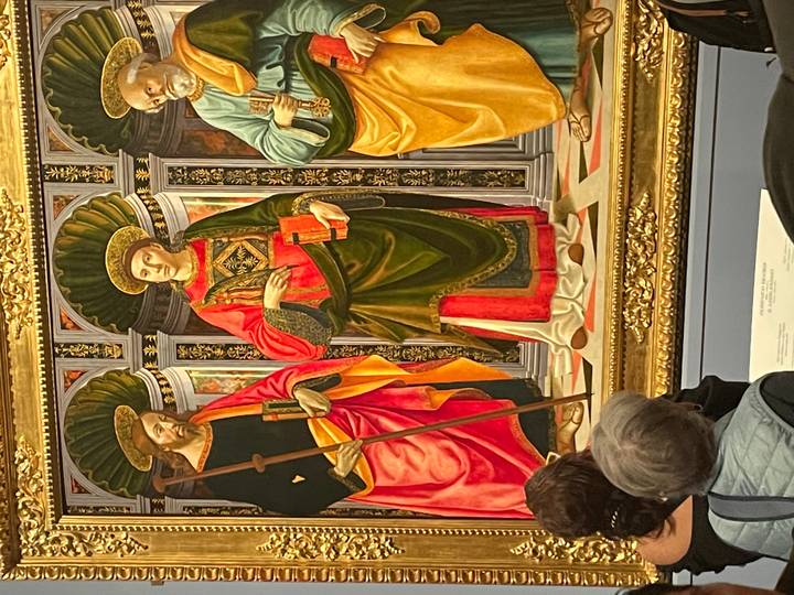 Visitors view a richly colored Renaissance painting showcased in an ornate gold frame.
