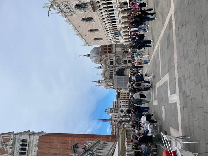 Crowds fill St. Mark’s Square with the basilica and Doge’s Palace under a bright, partly cloudy sky.