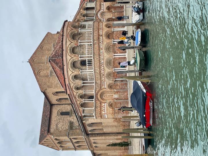 Boats line the dock in front of a Romanesque brick church on a quiet island canal.