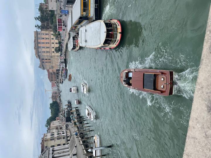 Boats and vaporettos navigate the Grand Canal beneath a gray Venetian sky viewed from a bridge.