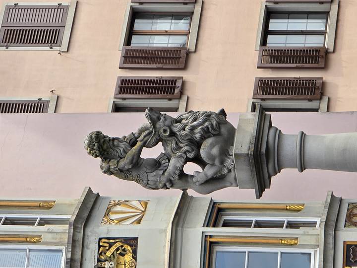 Stone fountain statue of a heroic figure wrestling a lion against pastel building façades