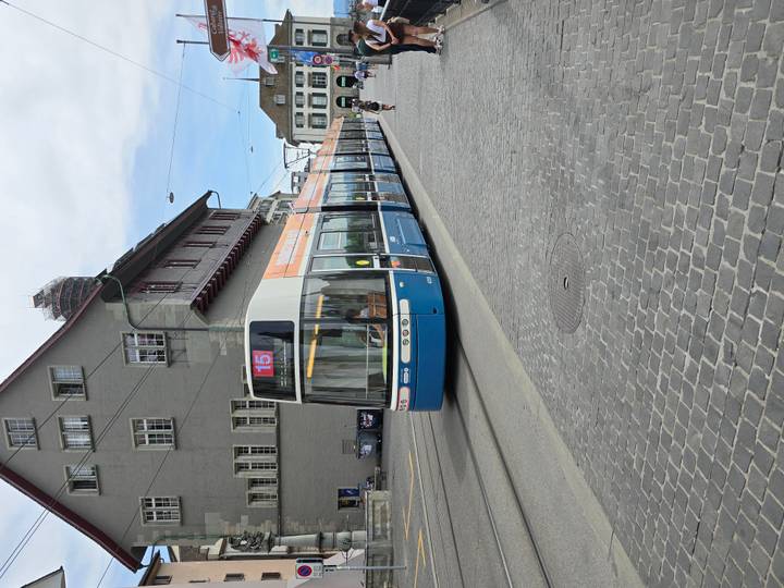 Blue and white Zurich tram number 15 travelling along cobblestone street beside grey civic building