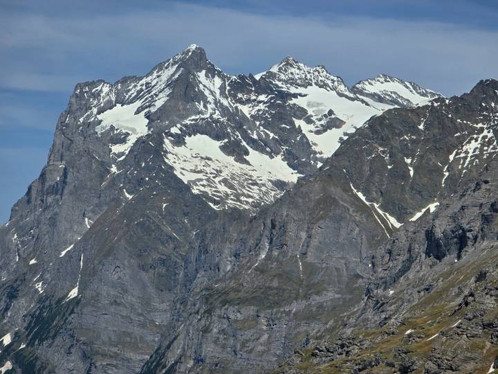 Jagged Swiss alpine massif with streaks of lingering snow under pale blue sky