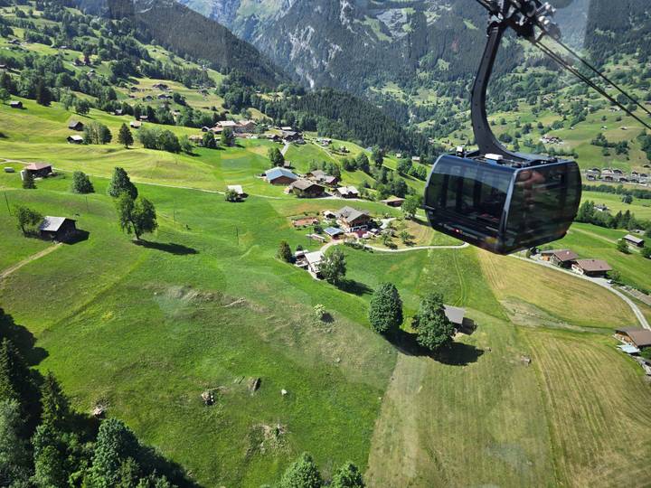Modern gondola cabin gliding above lush Swiss meadows and scattered chalets