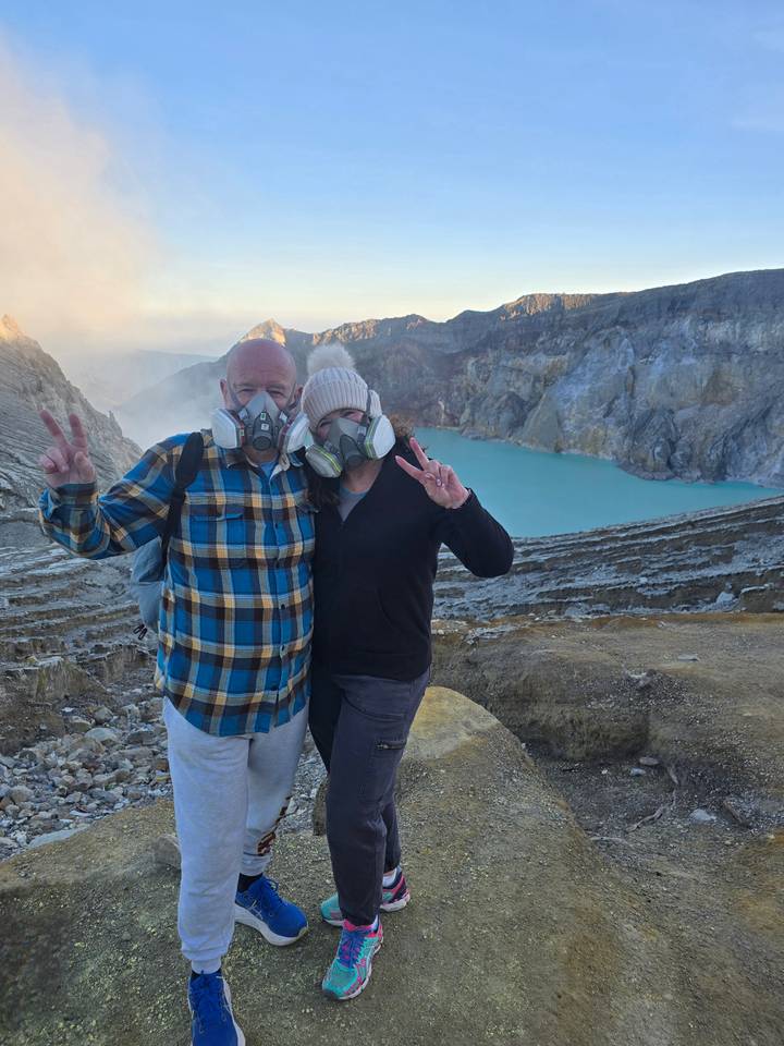 Travellers wearing respirators posing on crater rim with turquoise acid lake in background