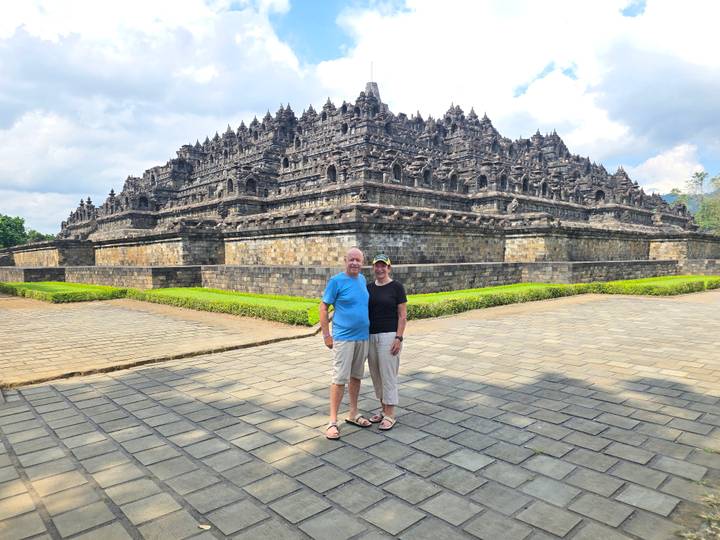 Couple standing in front of monumental stone terraces of Borobudur temple on sunny afternoon