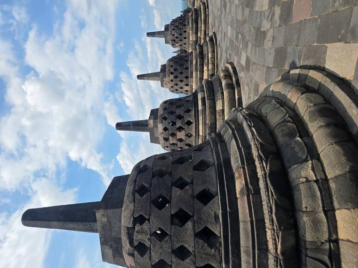 Row of bell-shaped stupas lining the upper terraces of Borobudur beneath scattered clouds
