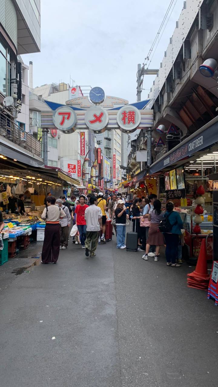 Animated crowd navigates a narrow market street lined with seafood stalls and bright vertical signs in Tokyo