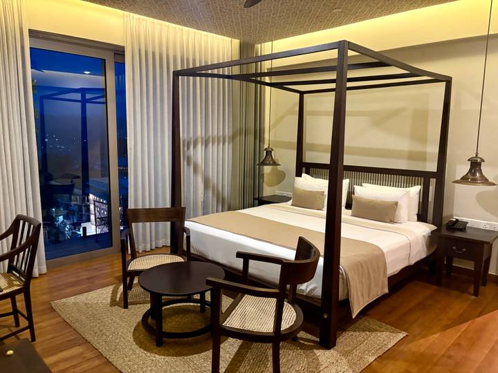 Modern hotel room with canopy bed, wooden floors and balcony window.