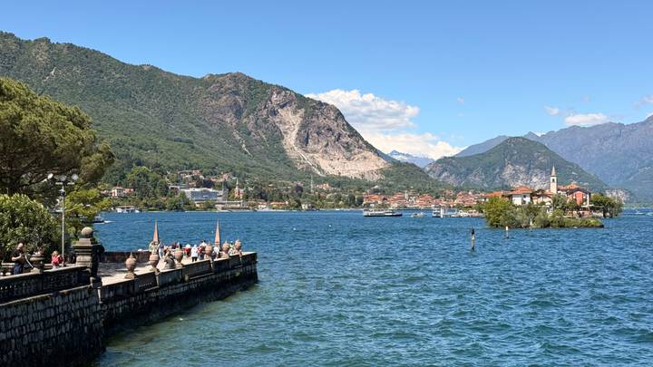 Visitors strolling along a lakeside promenade overlooking a vibrant town and surrounding mountains.