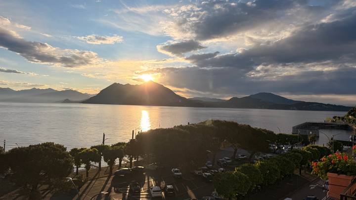 Sun setting behind a silhouetted mountain over calm lake waters with dramatic clouds.