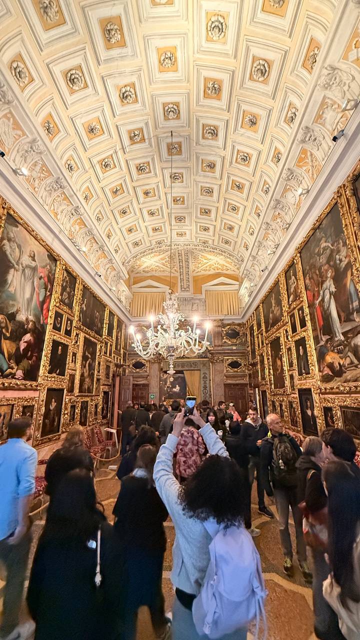 Lavish gallery hall filled with framed classical paintings and an ornate chandelier overhead.