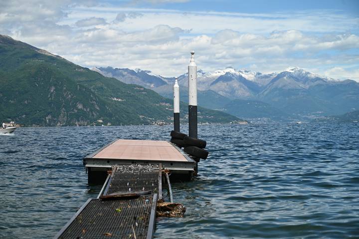 Small wooden pier stretching into a vast alpine lake surrounded by green and snow-capped peaks.