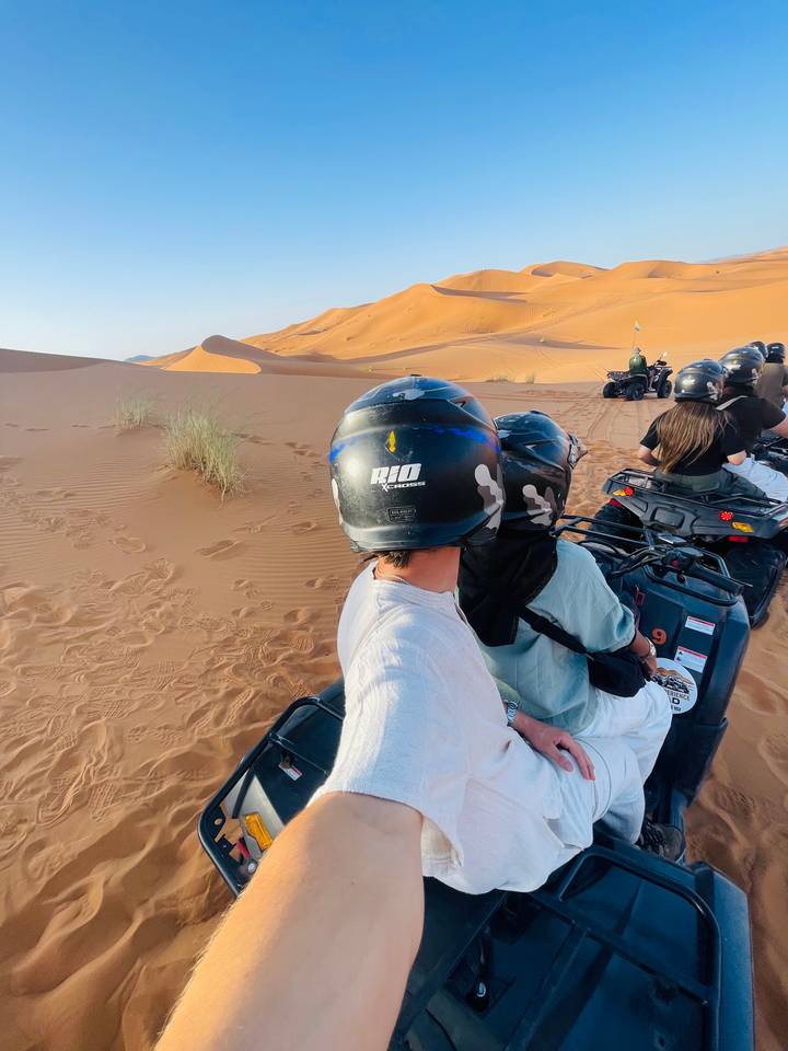 Tourists riding quad bikes single-file across rippled desert sand under clear sky.