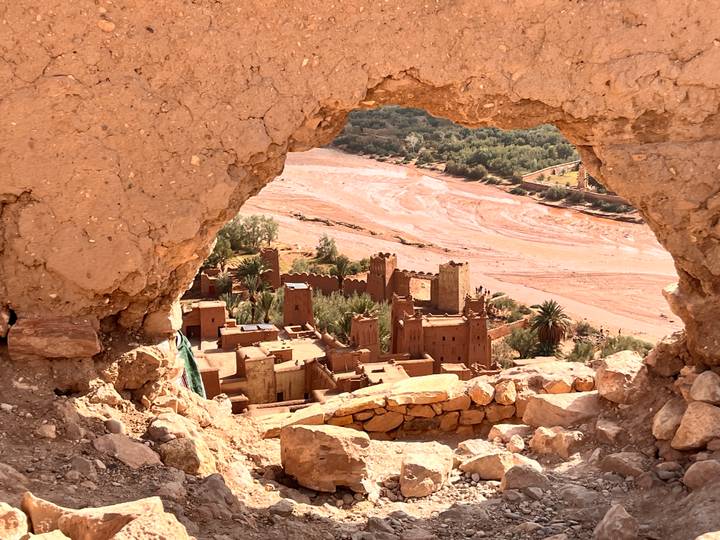 Clay kasbah village framed through a natural rock arch above a dry riverbed