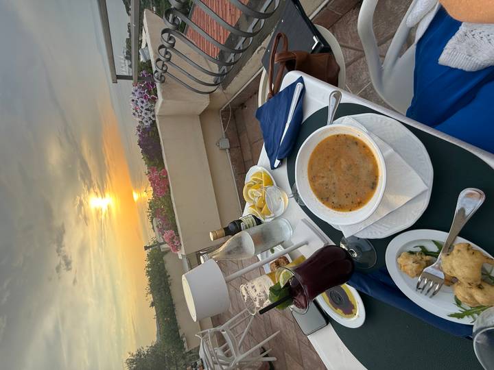 Outdoor dinner table set with soup, drinks and sea view at sunset on the Amalfi Coast