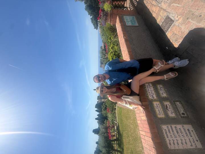 Couple poses against a brick wall overlooking colorful gardens and distant sea