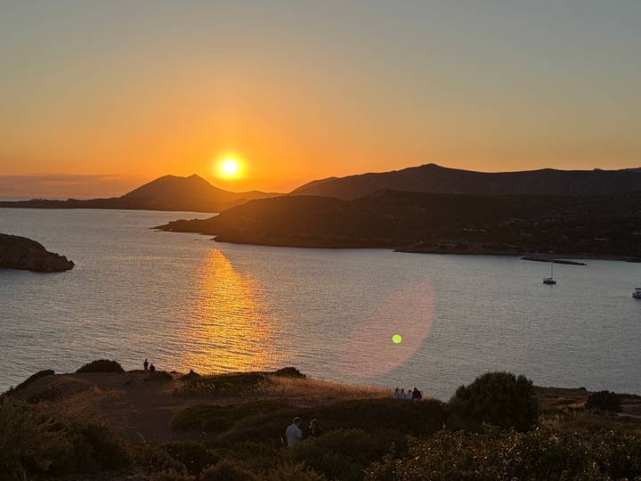 Brilliant orange sun setting over tranquil bay with silhouetted hills and sparkling water trail