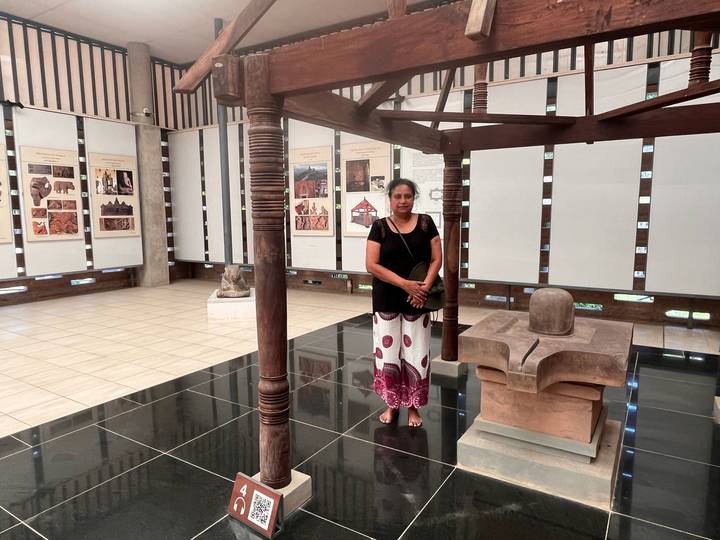 Visitor inside a museum gallery with informational panels and stone artifacts displayed on polished black floors.