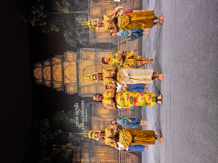 Traditional Apsara dancers in colorful costumes performing on a theatre stage set against an Angkor backdrop.
