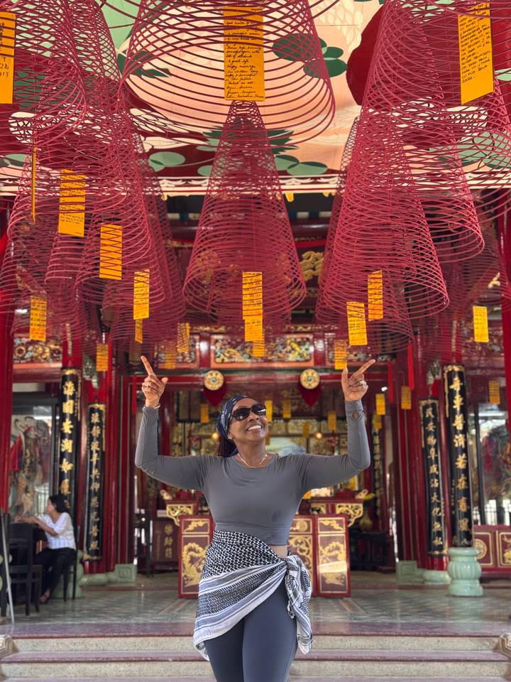 Visitor points upward beneath hanging red incense coils inside a vibrant Chinese temple.