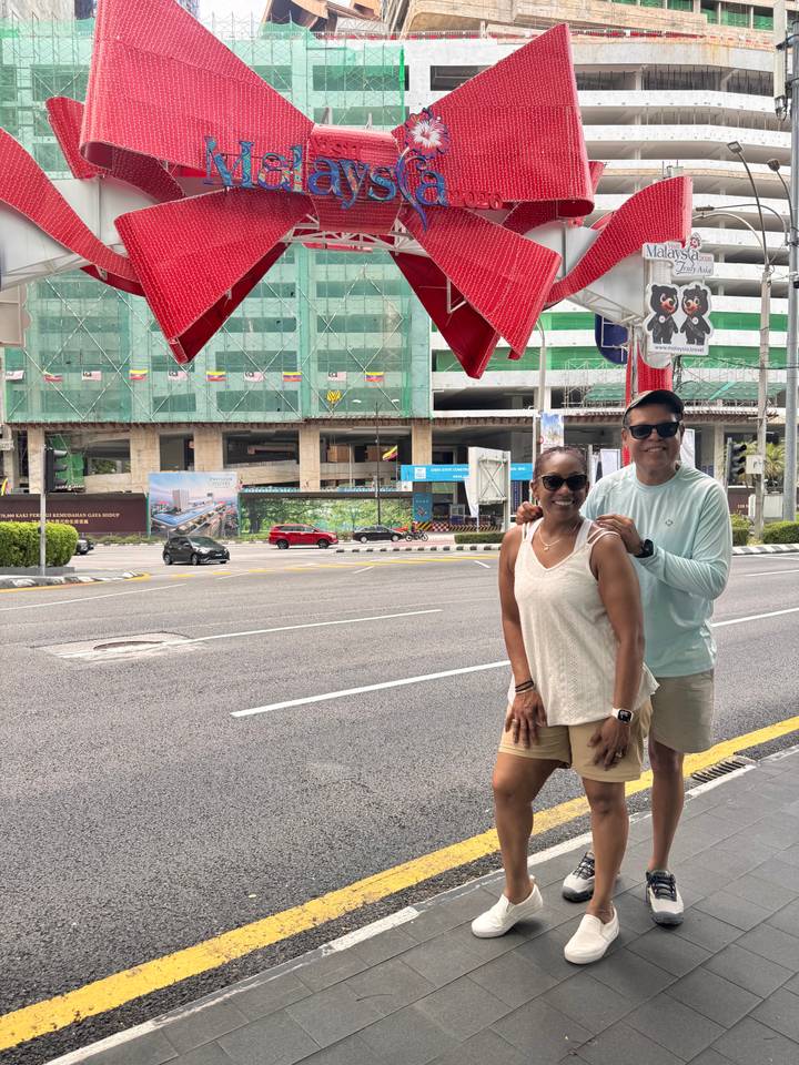 Couple poses on a busy Kuala Lumpur street with construction and green-netted high-rises in the background.