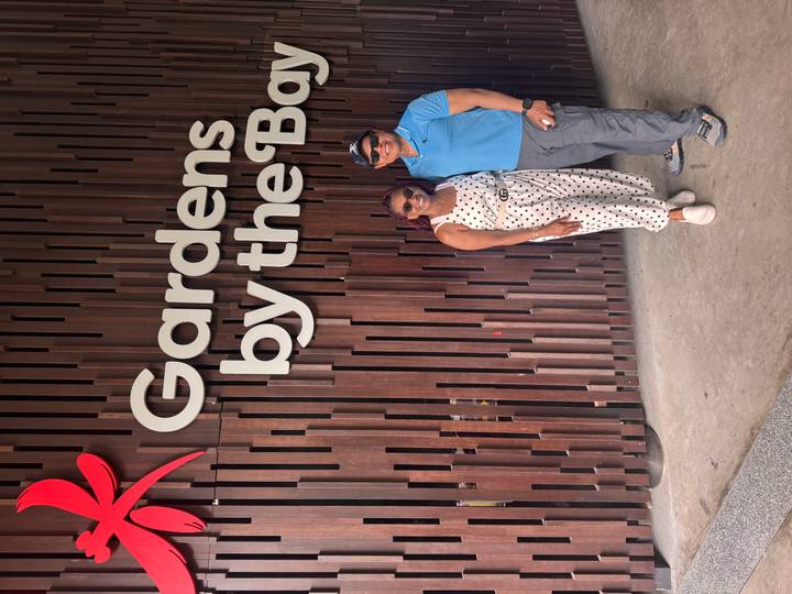 Couple smiling next to the wooden ‘Gardens by the Bay’ entrance sign.