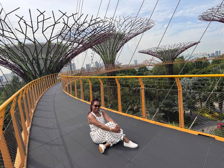 Traveller sits on the yellow-railed OCBC Skyway walkway with Supertrees and city skyline in the background.