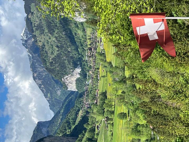Verdant Swiss valley dotted with farms and framed by high alpine cliffs, Swiss flag in foreground