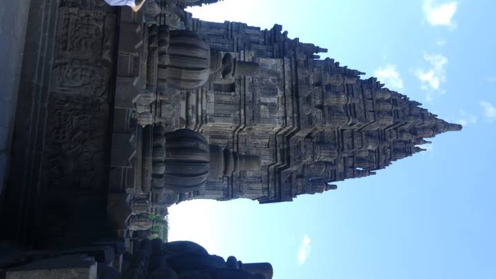 Detailed stone spire of a Prambanan temple rises sharply against a blue sky